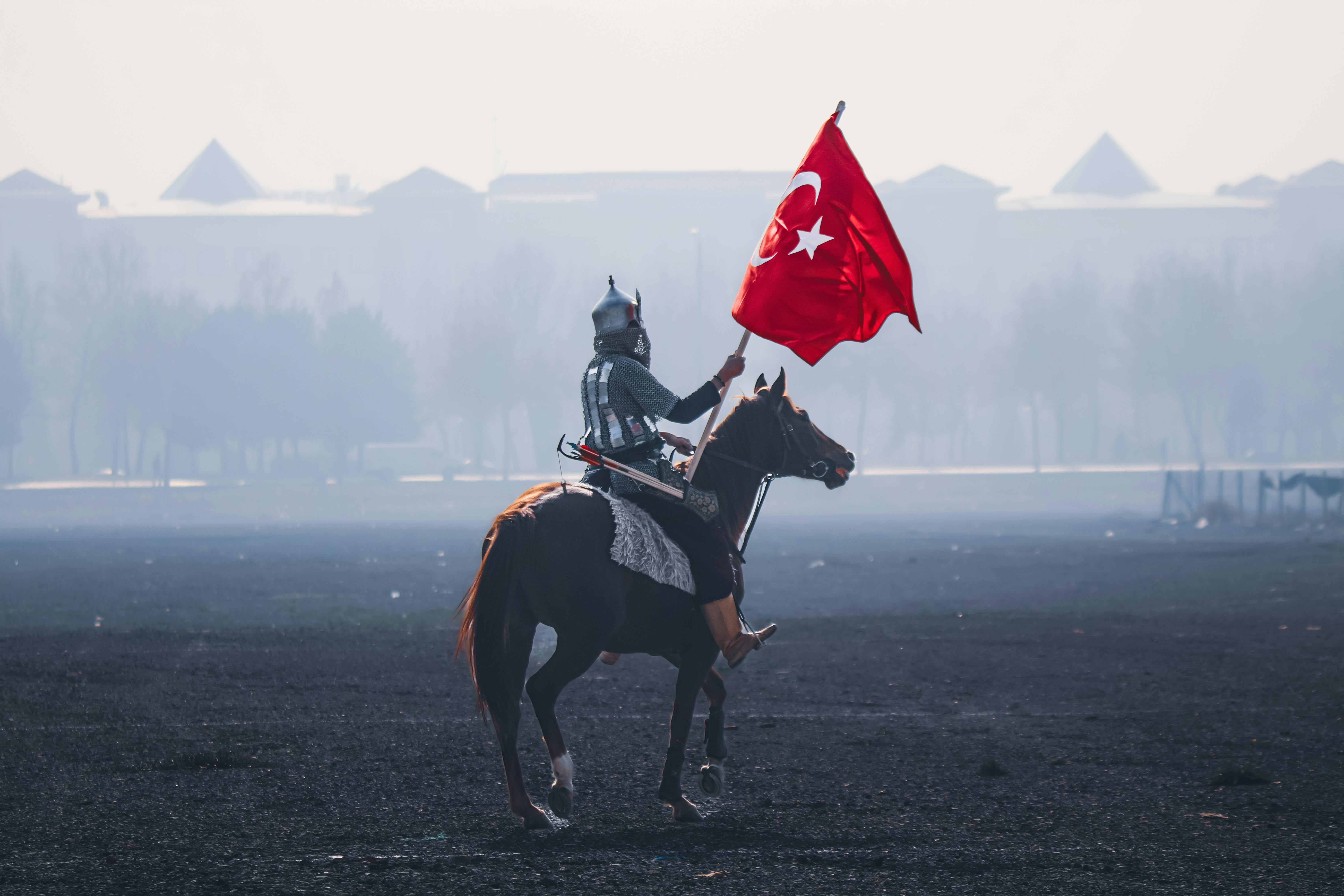 A horseman in traditional armor holding the Turkish flag, riding in an open field in Konya, Türkiye.