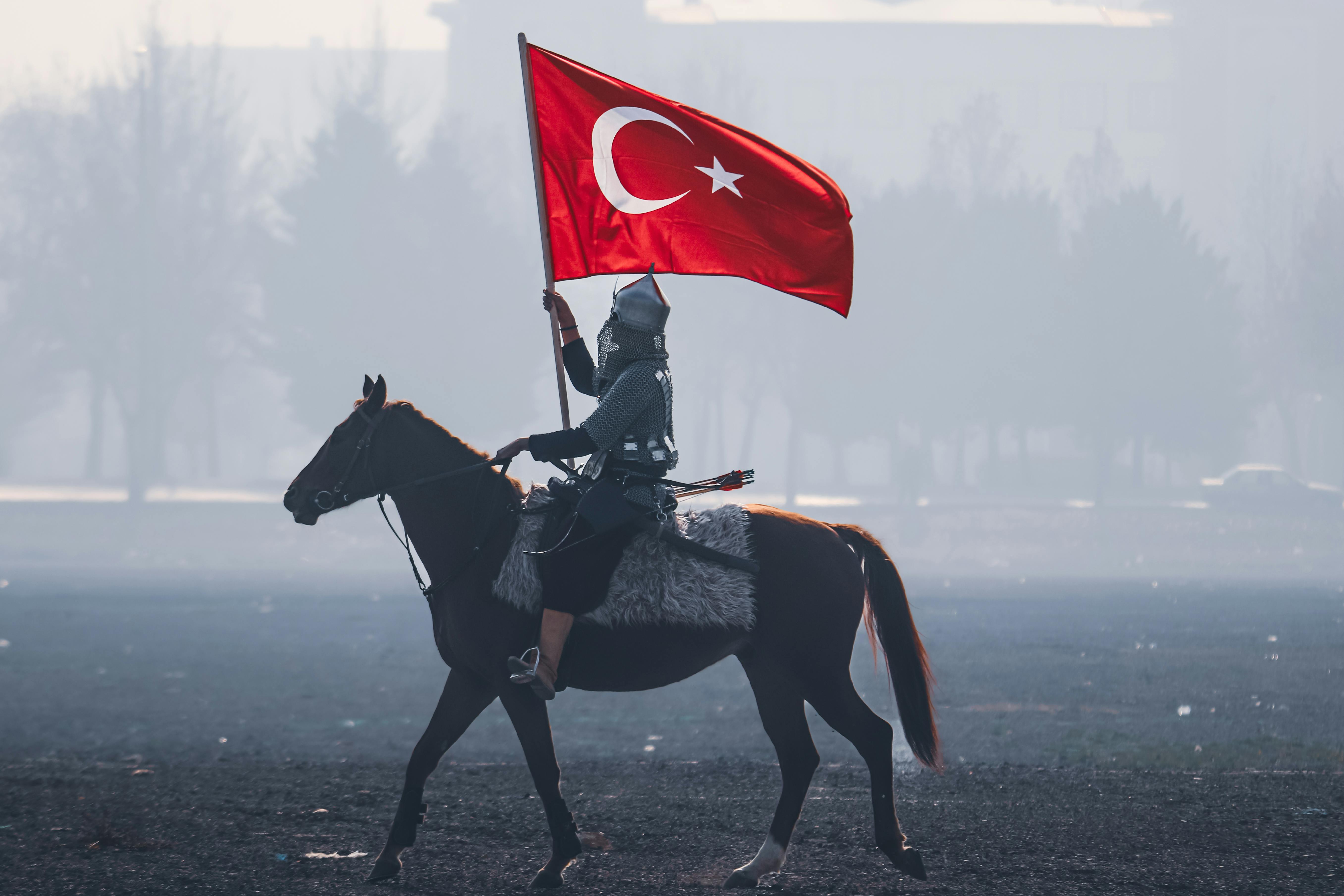 A horseman in traditional attire holding the Turkish flag rides through a misty field in Konya, Türkiye.