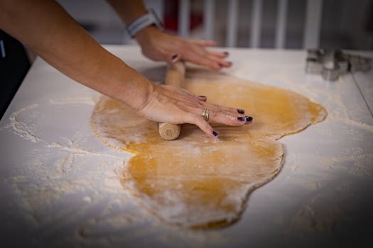 Hands rolling dough with a wooden pin on a floured surface, ready for baking.