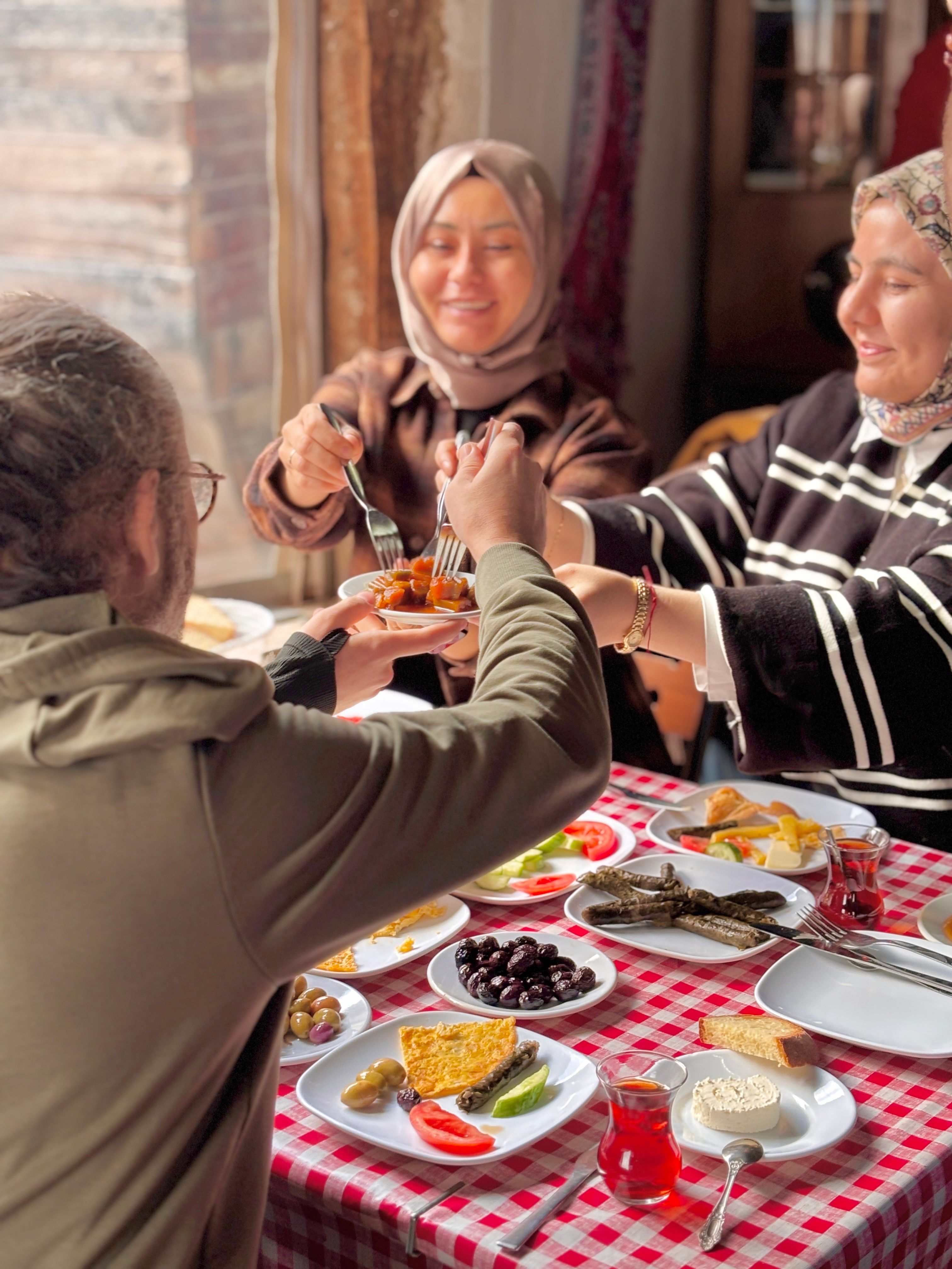 Three friends sharing a traditional breakfast with various dishes on a checkered table.