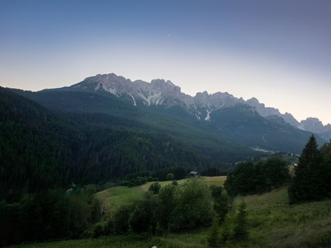 Picturesque sunset over the Dolomites from Candide, Veneto, showcasing lush greenery and towering peaks.