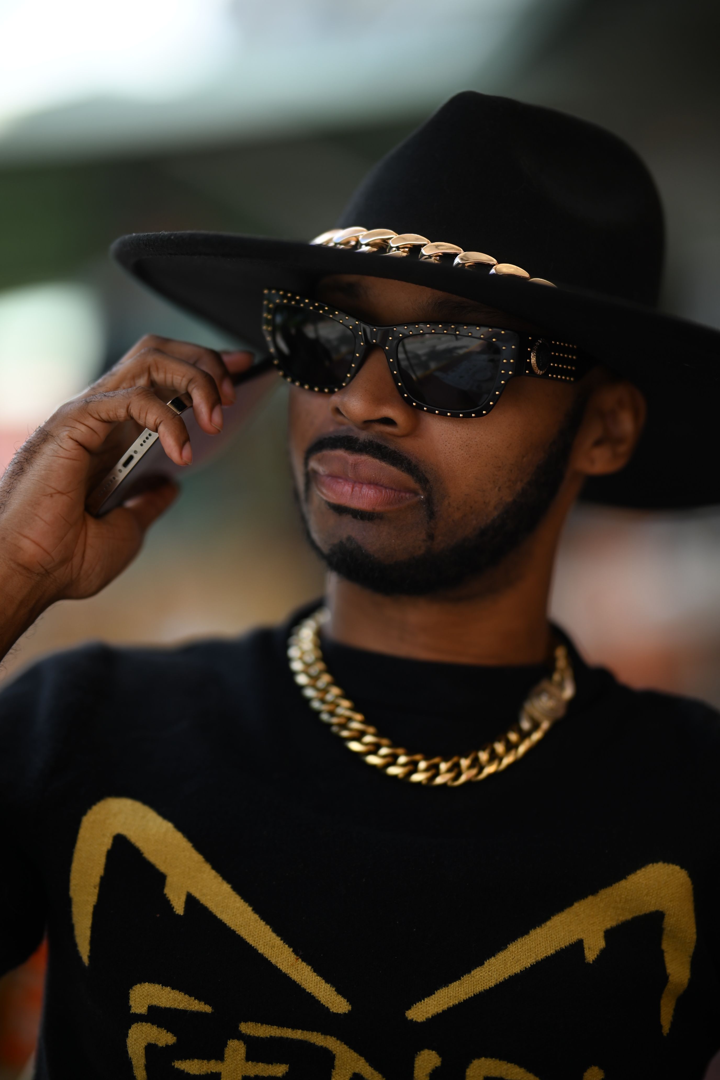 Stylish man wearing a black hat and sunglasses, holding a phone in Miami.