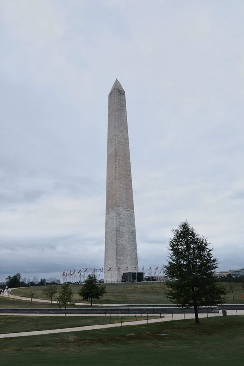 Free The Washington Monument in Washington, DC, under a cloudy sky, surrounded by flags. Stock Photo