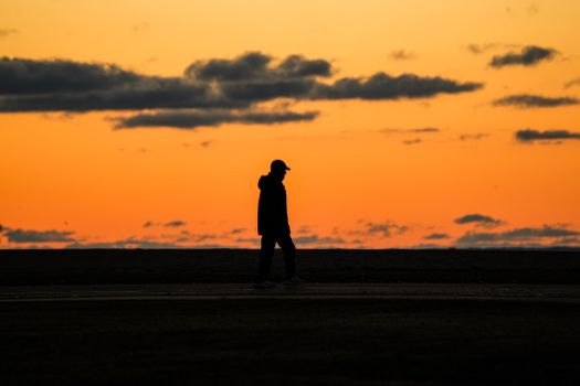 Silhouette of a man walking against a vivid orange sunset sky, creating a dramatic scene.