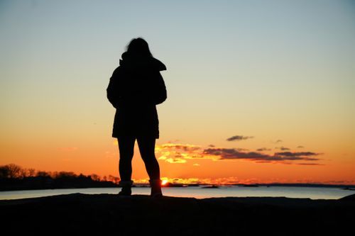 Free Silhouette of a person standing by the sea during a vibrant sunset. Stock Photo