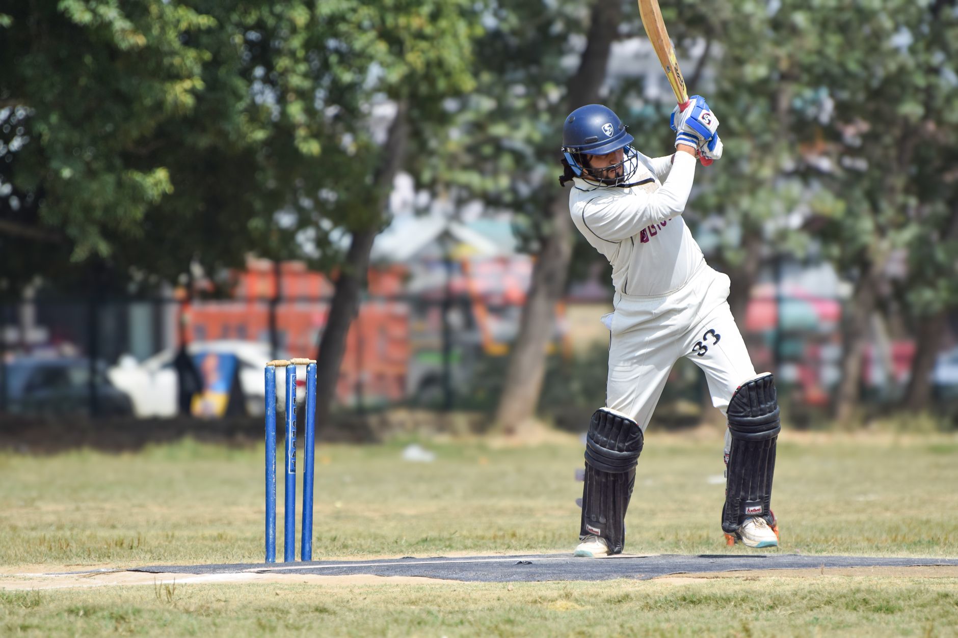 A cricketer in white attire ready to bat on a sunny outdoor field.