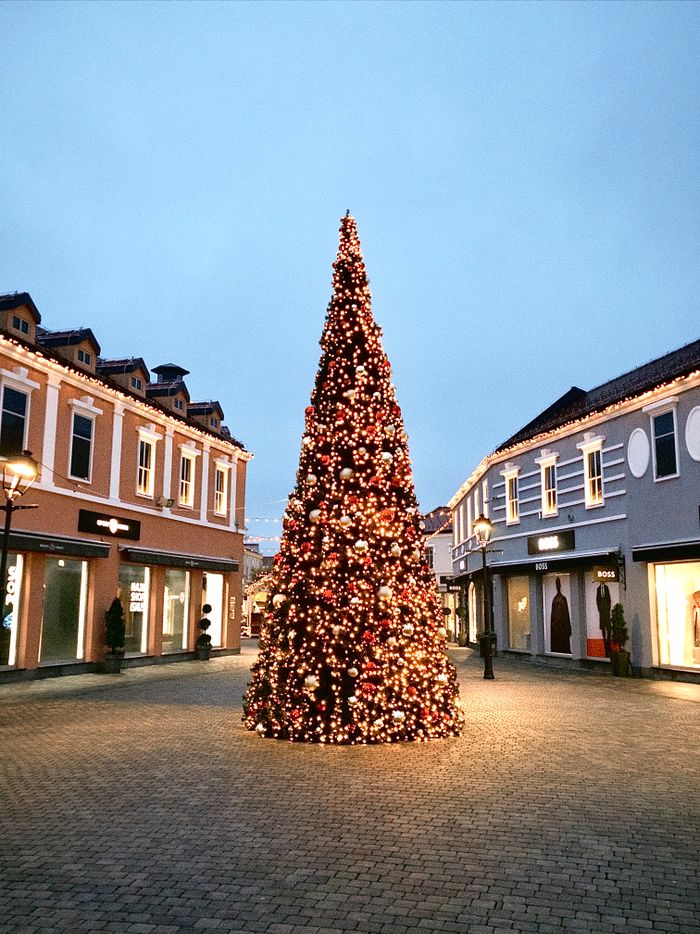Outdoor shopping plaza lit up with a large Christmas tree and storefront lights