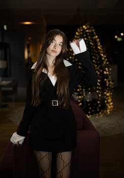 Stylish woman in black outfit posing indoors with a Christmas tree in the background.
