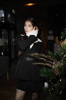 Stylish woman posing elegantly indoors next to decorated Christmas tree.
