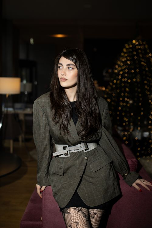 Free Stylish woman in a modern suit poses in a cozy, dimly lit interior with holiday lighting. Stock Photo