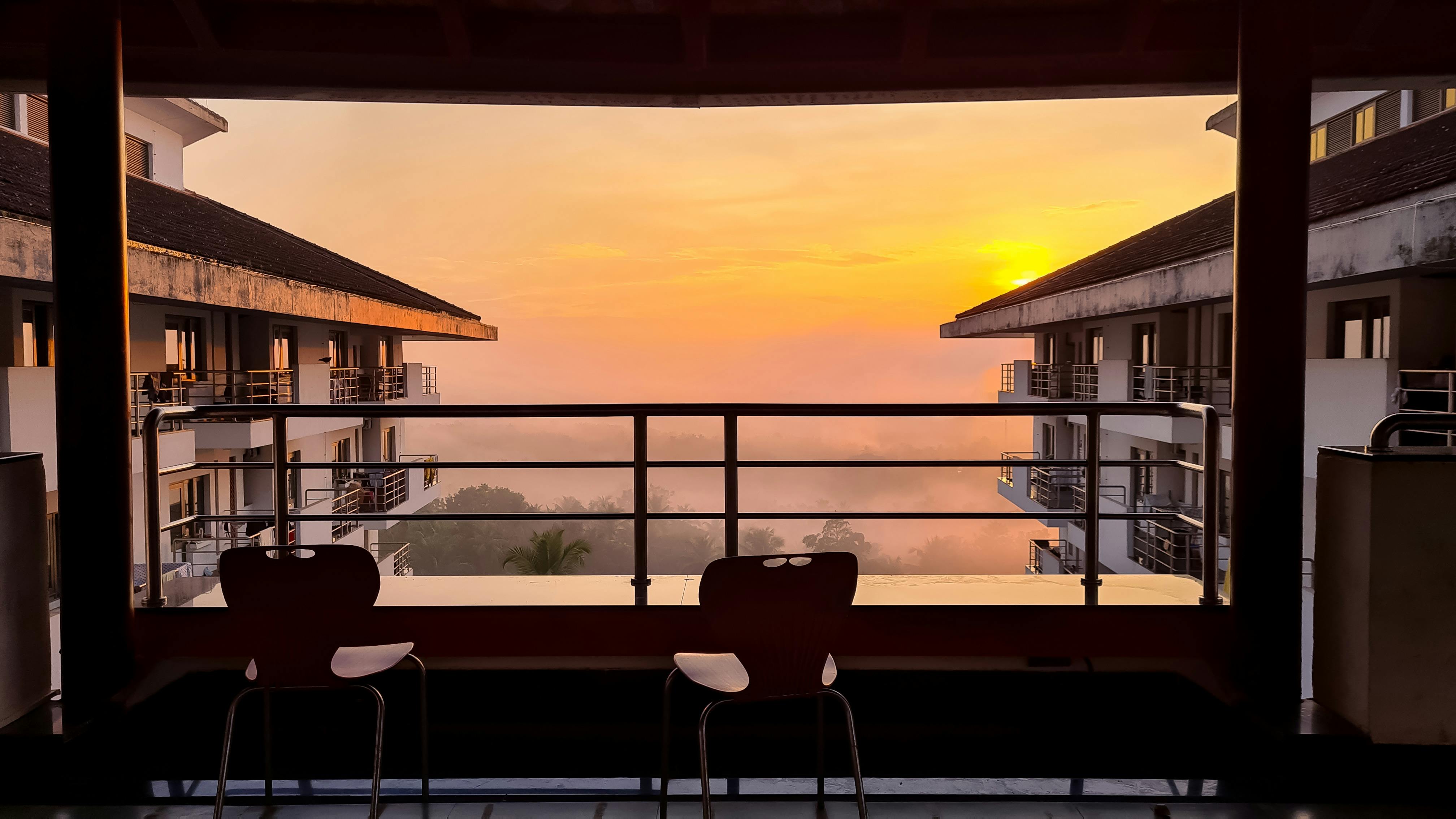 Silhouette of chairs at a balcony with a breathtaking sunset view between buildings.