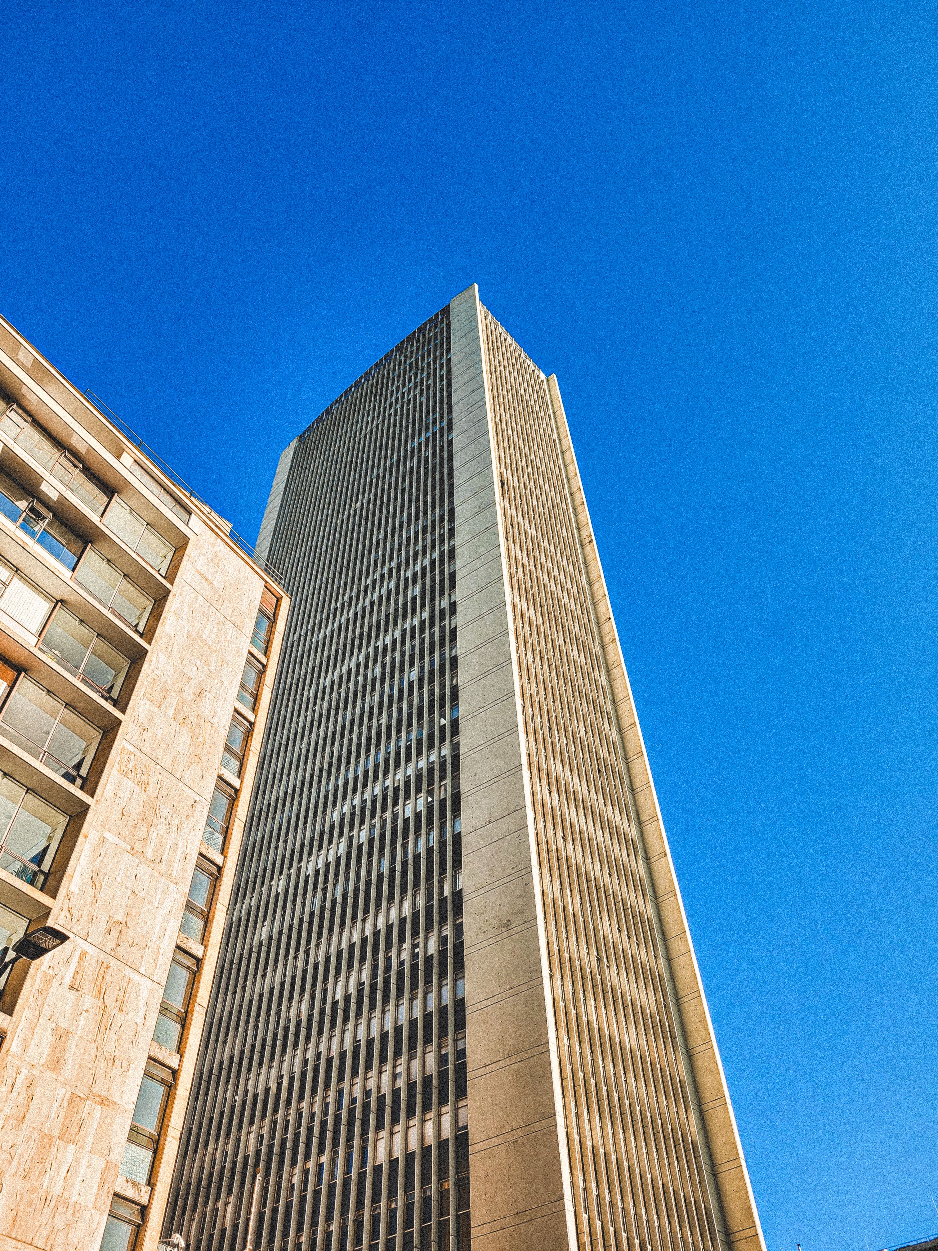 Kostenlos Ein markanter, moderner Wolkenkratzer ragt vor einem leuchtend blauen Himmel empor und präsentiert urbane Architektur. Stock-Foto