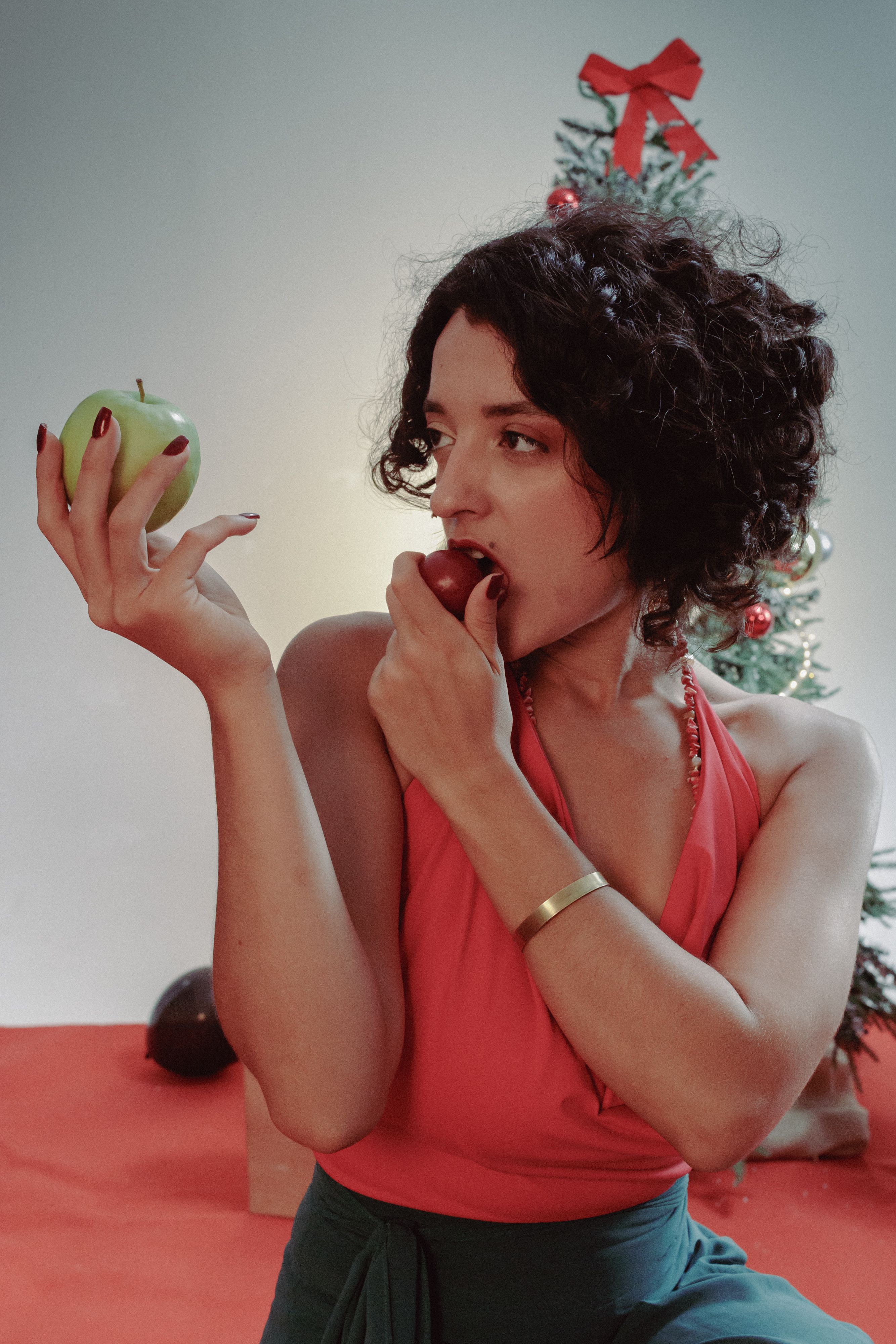 A woman in a festive setting holding a green apple and eating a red apple.