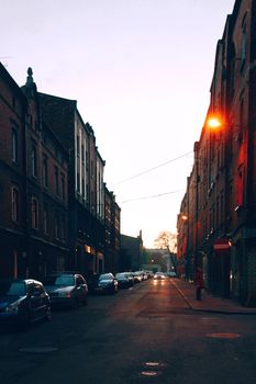 A dimly lit street in Katowice, Poland, captured at twilight with cars parked along brick buildings.