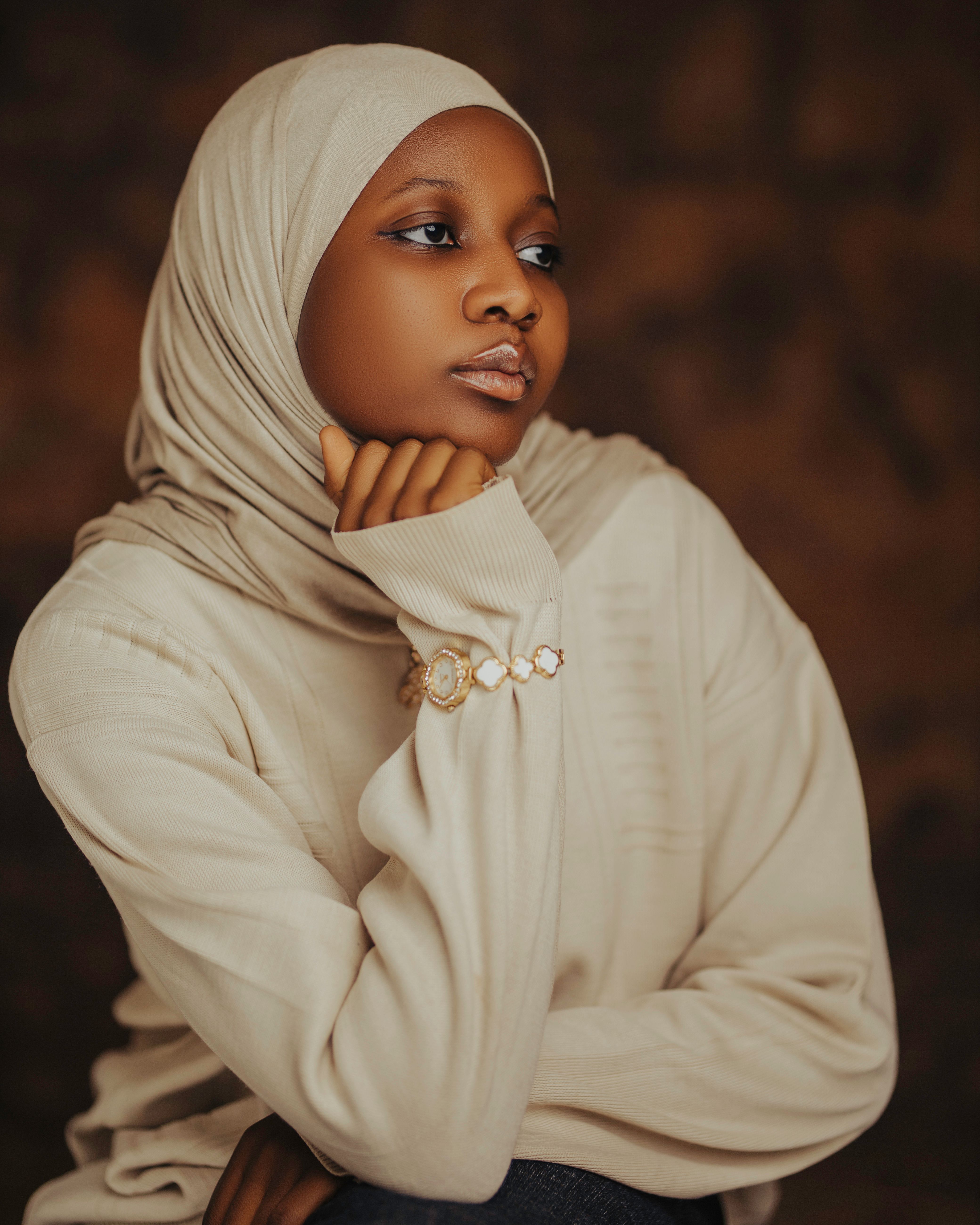 A contemplative young woman in a beige hijab with a soft neutral background.