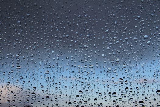Close-up of water droplets on a window with a cloudy sky in the background, capturing a serene, rainy ambiance.