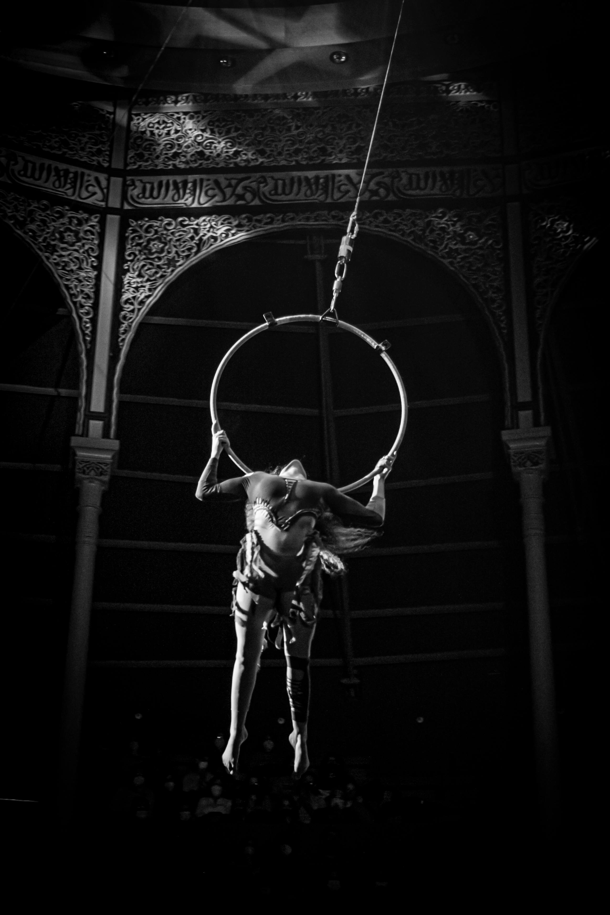 Free Black and white photo of an aerial acrobat performing on a hoop in a theater setting. Stock Photo