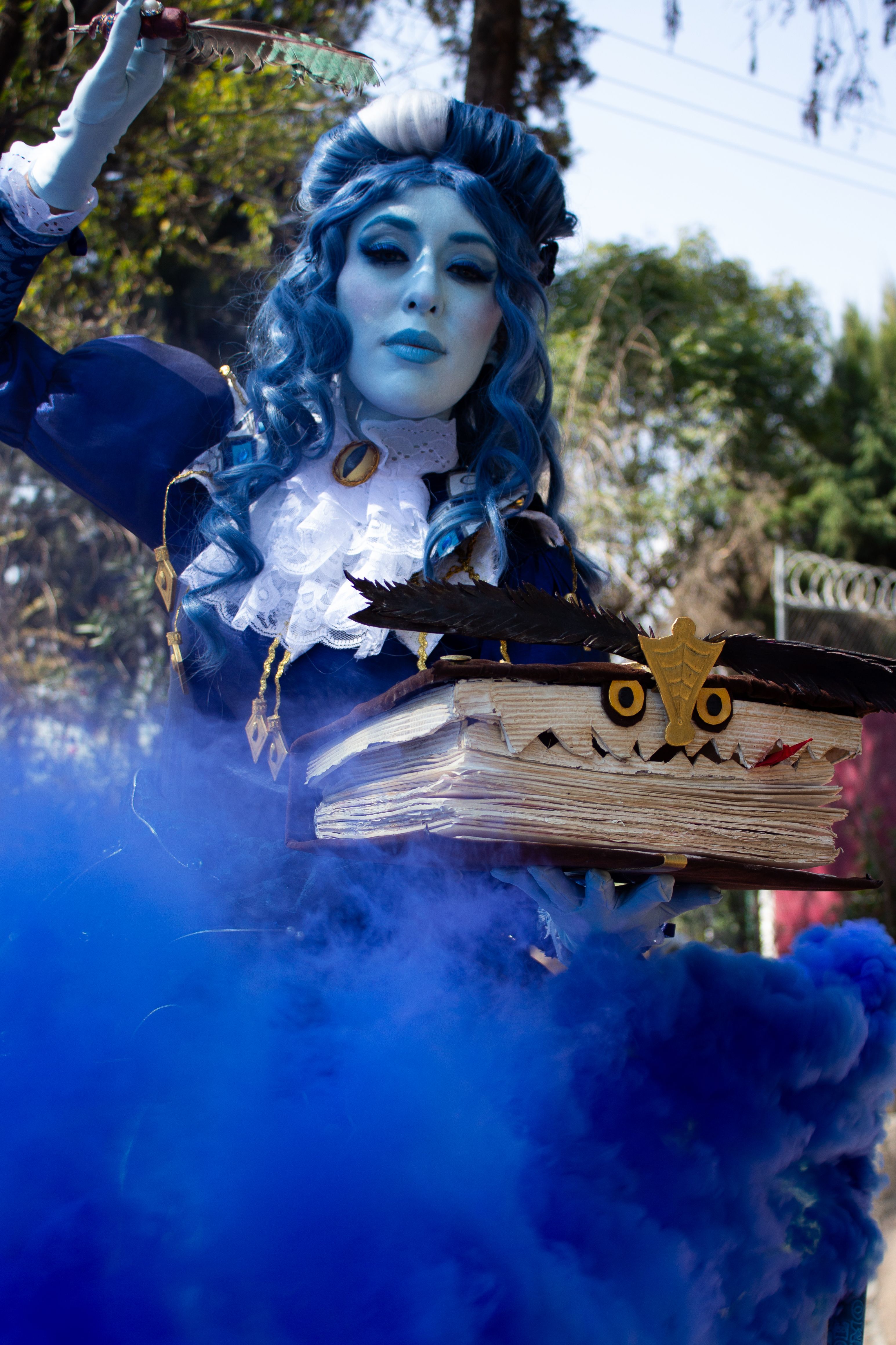 Mystical character in blue fantasy attire holding a spellbook with eerie smoke.