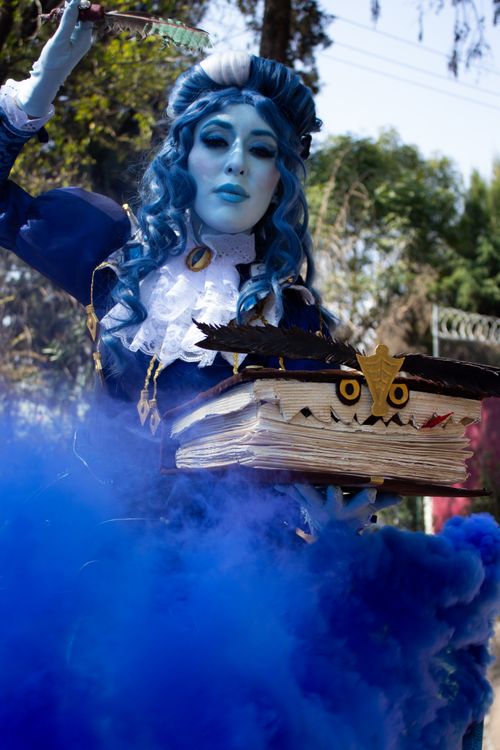 Free Mystical character in blue fantasy attire holding a spellbook with eerie smoke. Stock Photo