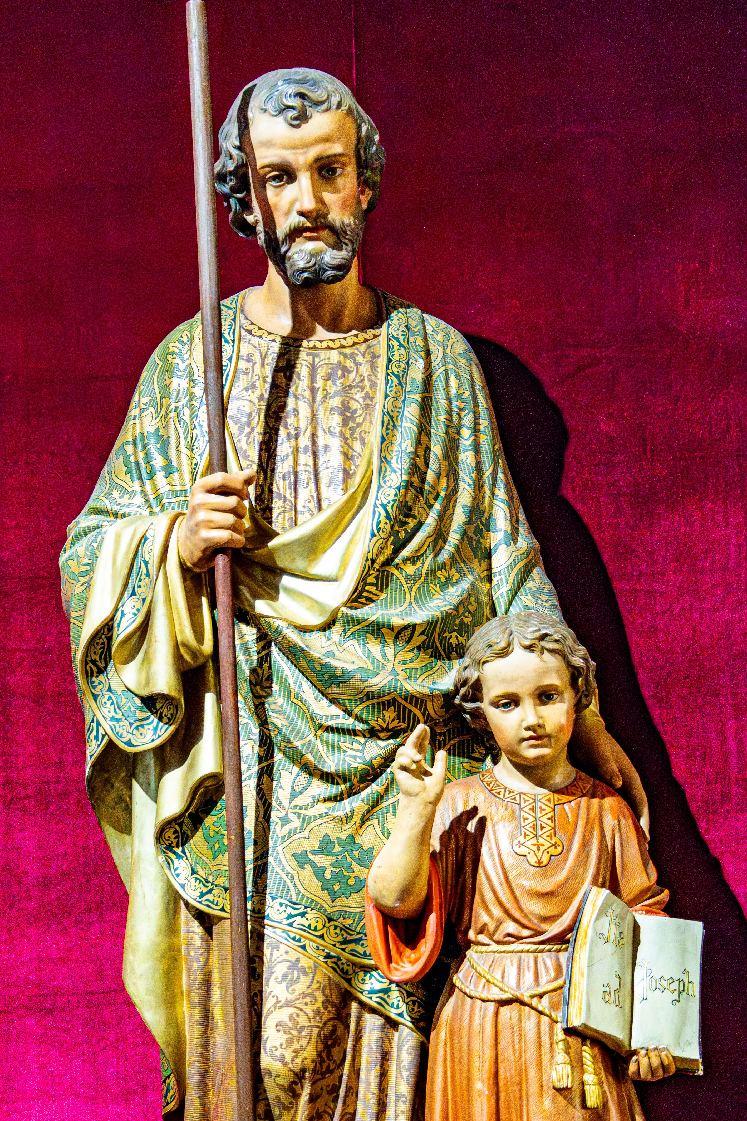 Colorful statue of Saint Joseph with child in Nazareth, Israel, set against a rich velvet background.