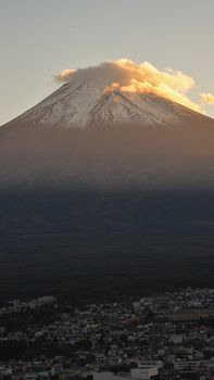 Stunning twilight view of Mount Fuji, Japan, with cloud-covered peak overlooking a cityscape.
