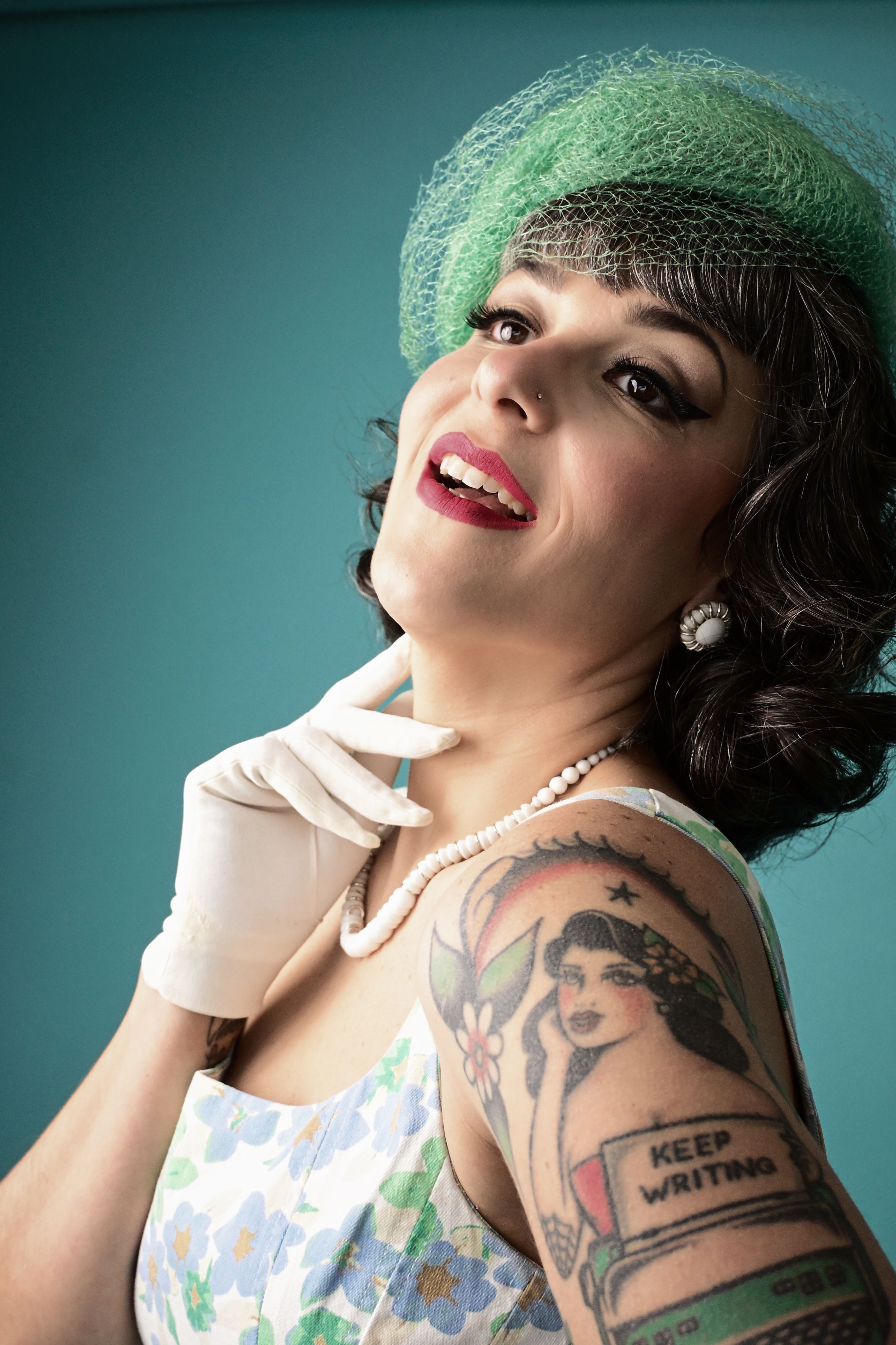 Woman in 1950s vintage style showcasing tattoo art with a confident pose.