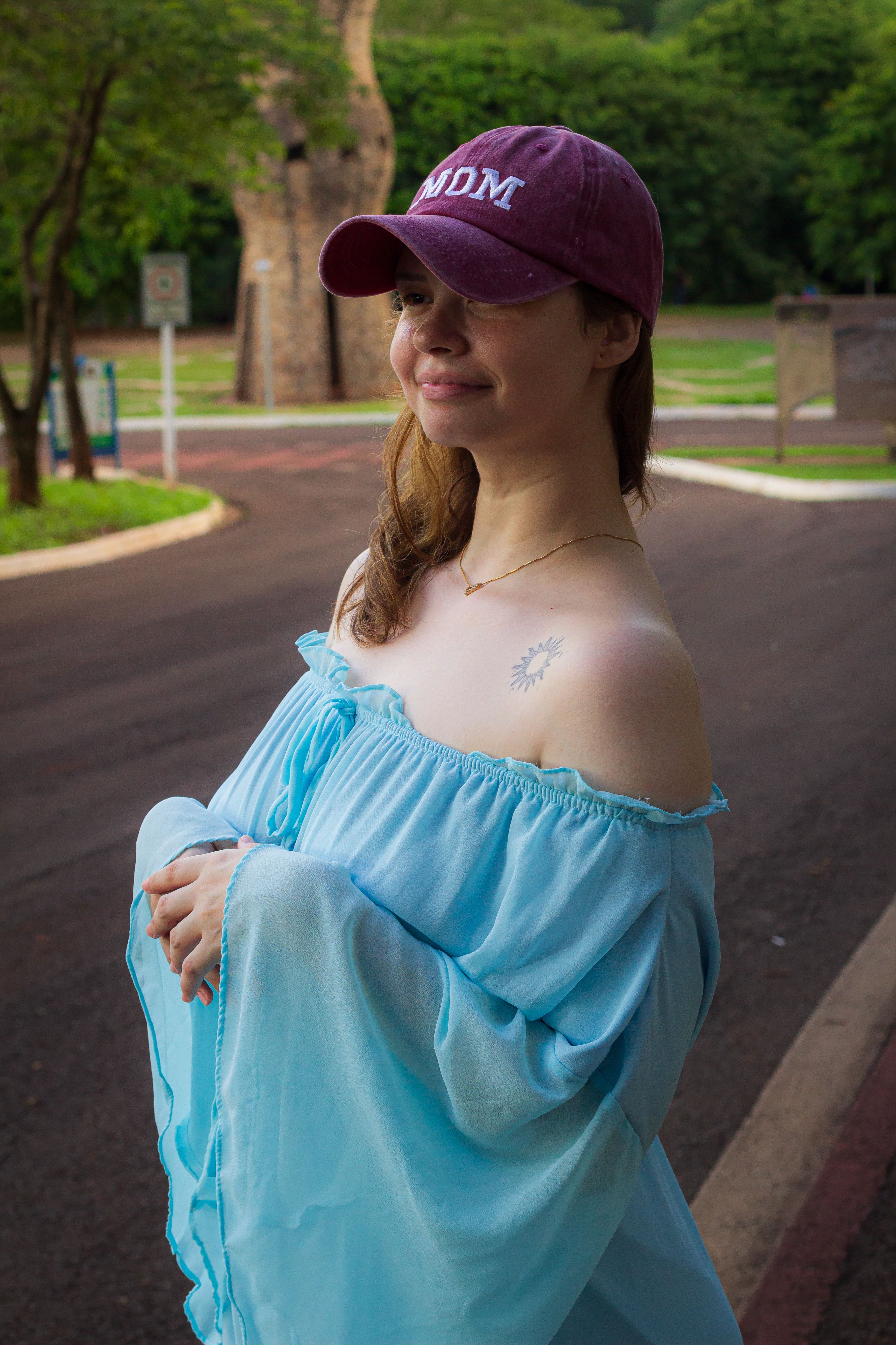 A young woman in a blue dress and cap enjoys a day outdoors in Campo Grande.