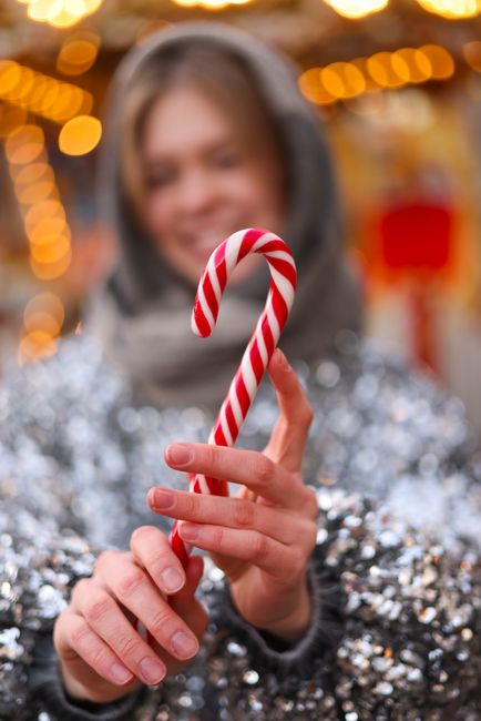 Festive scene with a blurred woman holding a candy cane surrounded by lights.