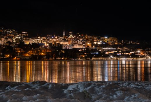 A stunning night view of St. Moritz with snow and reflections on the lake.
