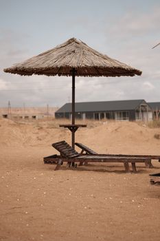 Empty rustic beach loungers under a straw parasol on a sandy coast.