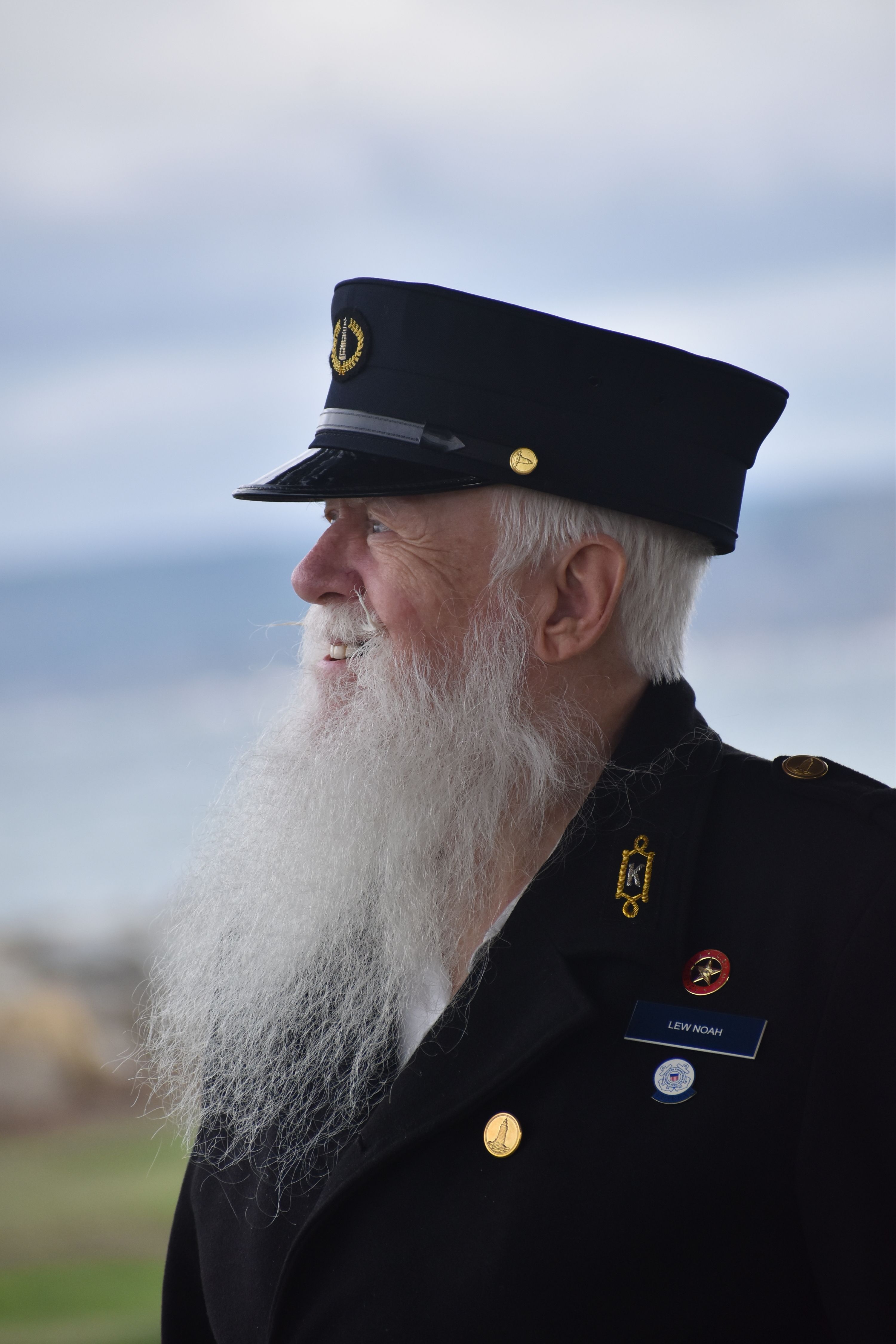 Elderly sailor in uniform with a long beard looks over the sea, showcasing experience and wisdom.