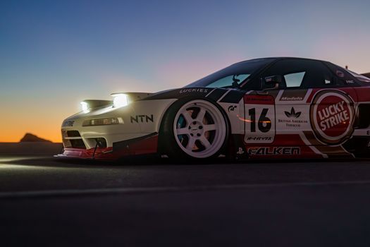 A sleek racing car with branded decals against a vibrant sunset backdrop on an open road.