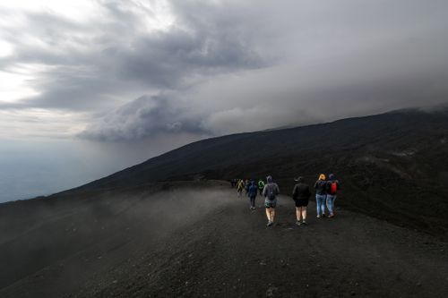 Free Group of people hiking on a volcanic landscape under a dramatic cloudy sky, creating a moody atmosphere. Stock Photo