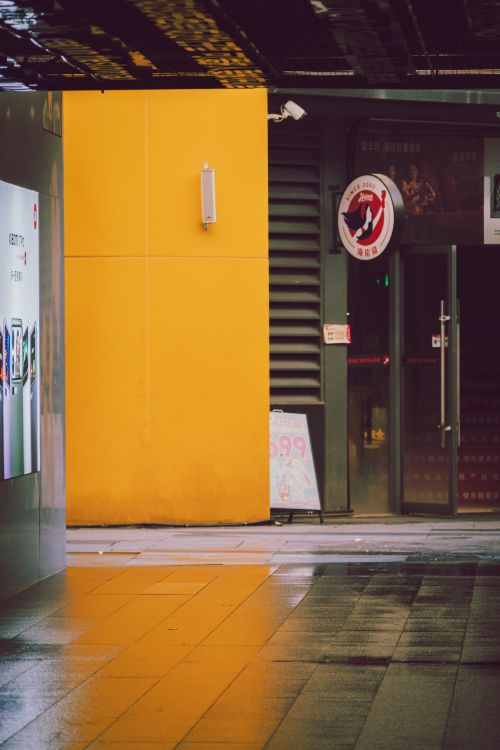 Free Vibrant urban street scene featuring a bright yellow wall and wet pavement. Stock Photo