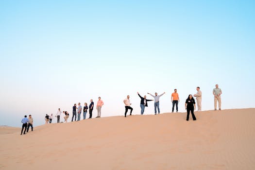 A group of adults standing on a desert sand dune during sunset, enjoying the serene landscape.