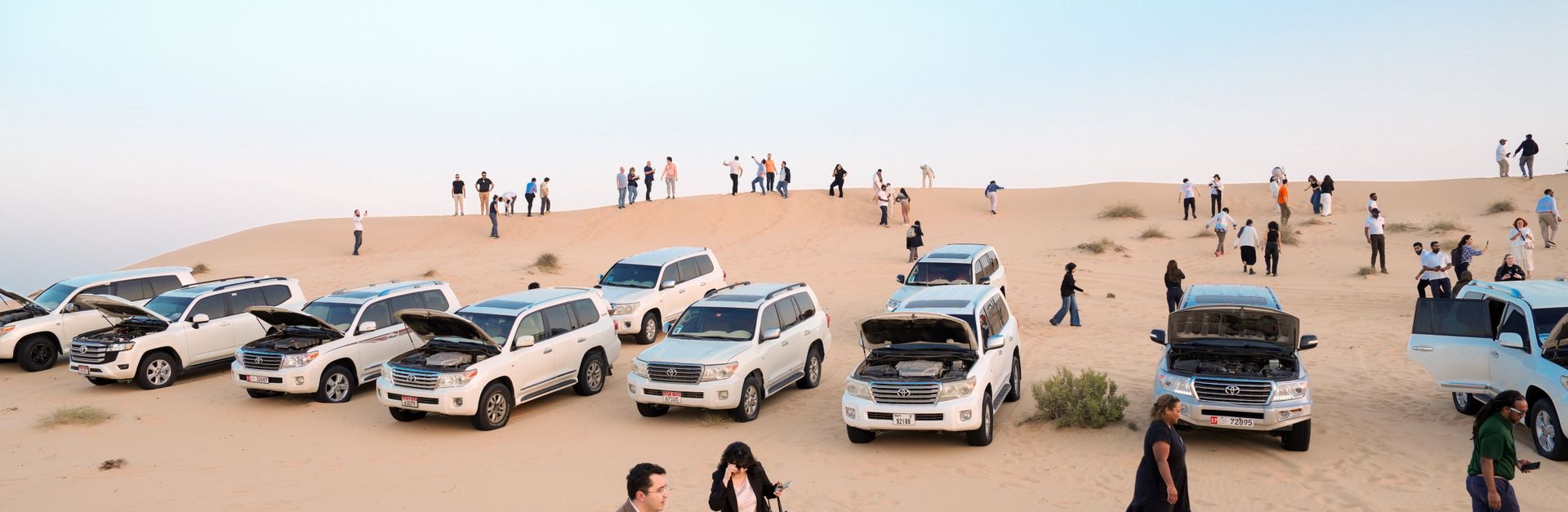 A group of tourists and SUVs on a sandy desert dune during daytime.