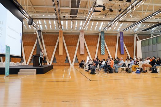 Large indoor conference with audience focused on a speaker presenting from a podium.