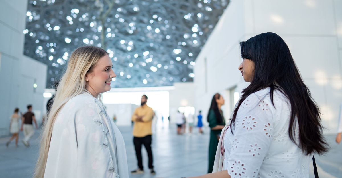 A candid shot of two women having a conversation inside a contemporary museum setting.