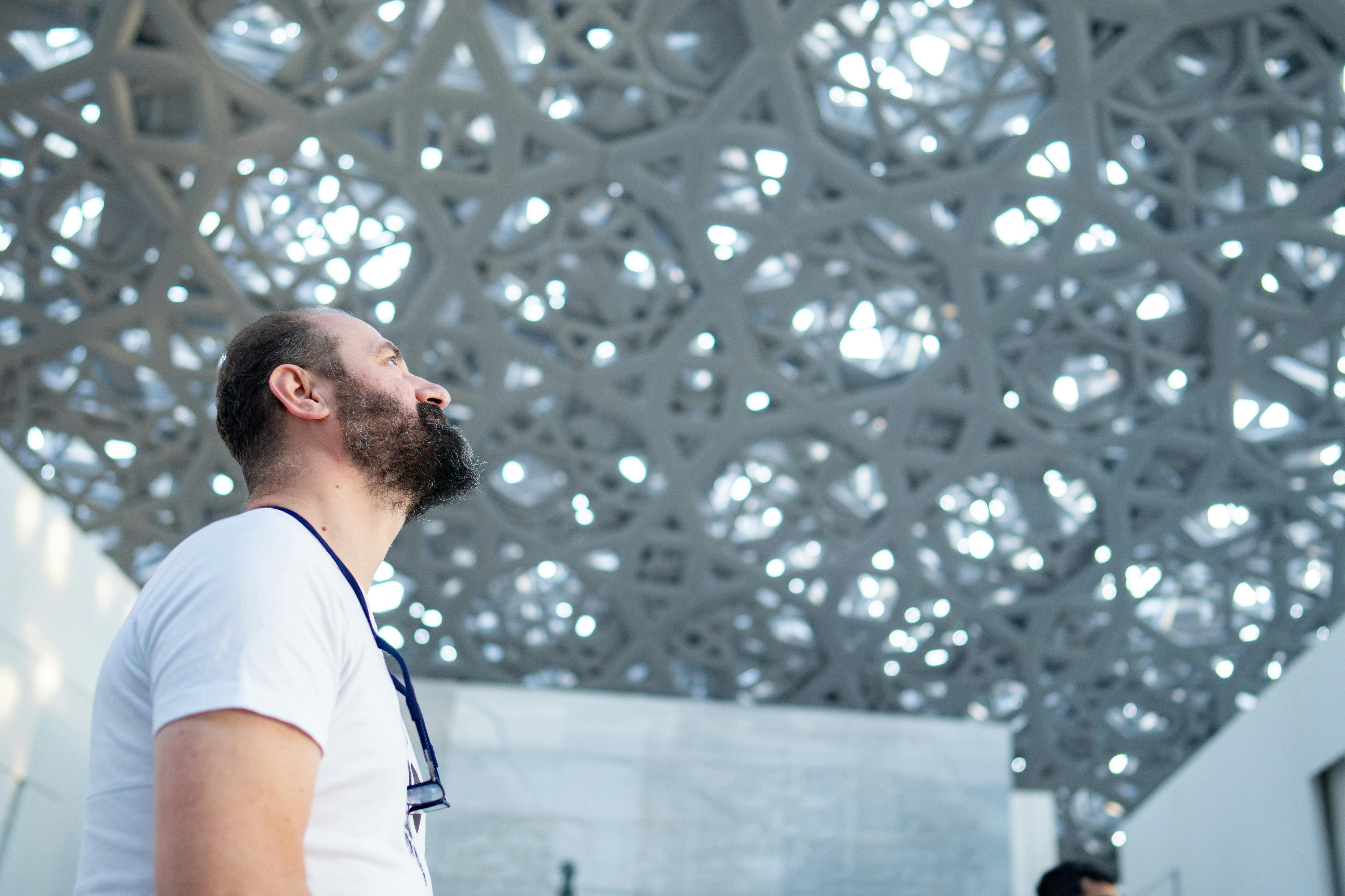 A man admiring the intricate ceiling design of a modern museum indoors.
