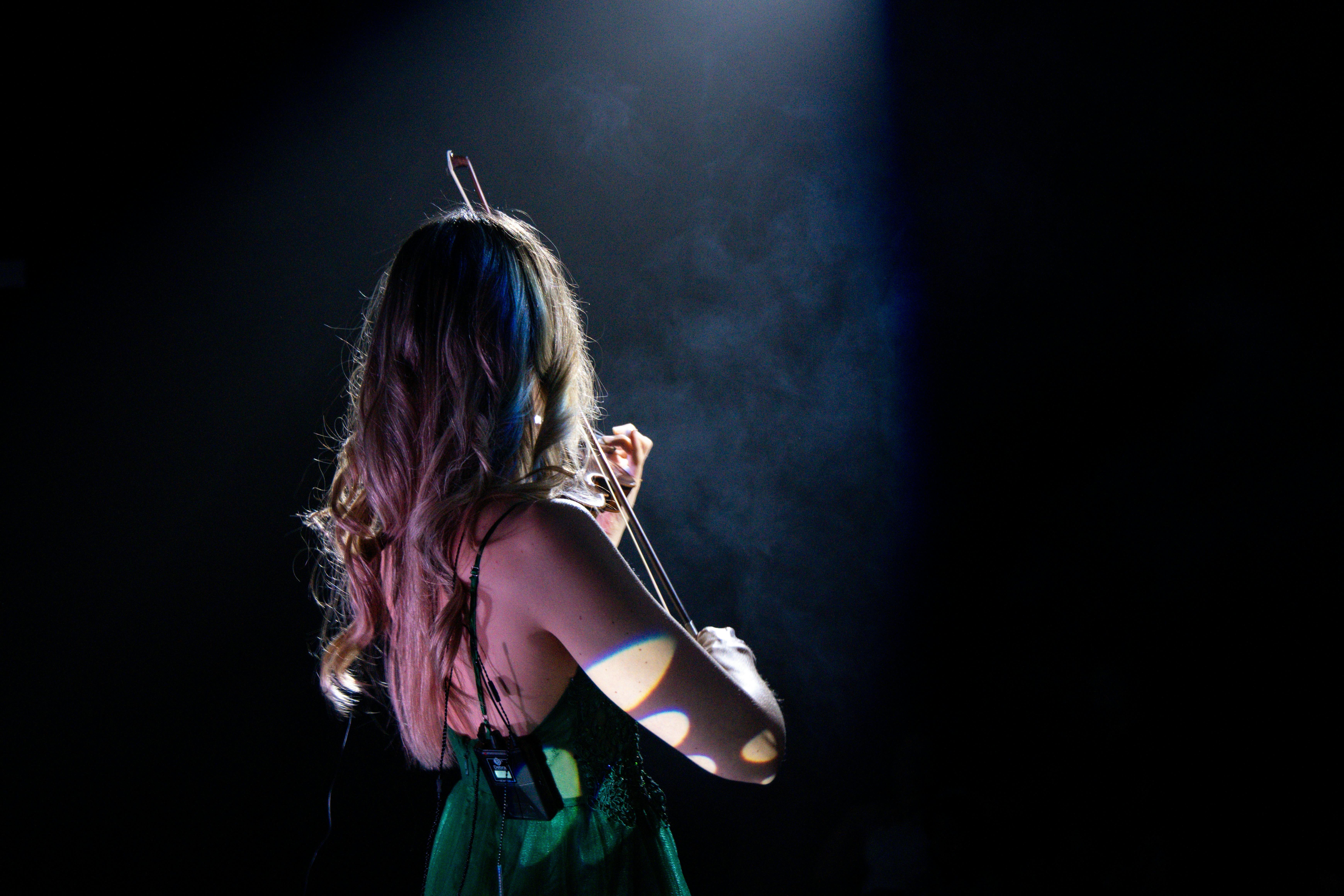 Ilmainen Vihreään mekkoon pukeutunut naisviulisti soittaa intohimoisesti kohdevalon alla. Kuvapankkikuva