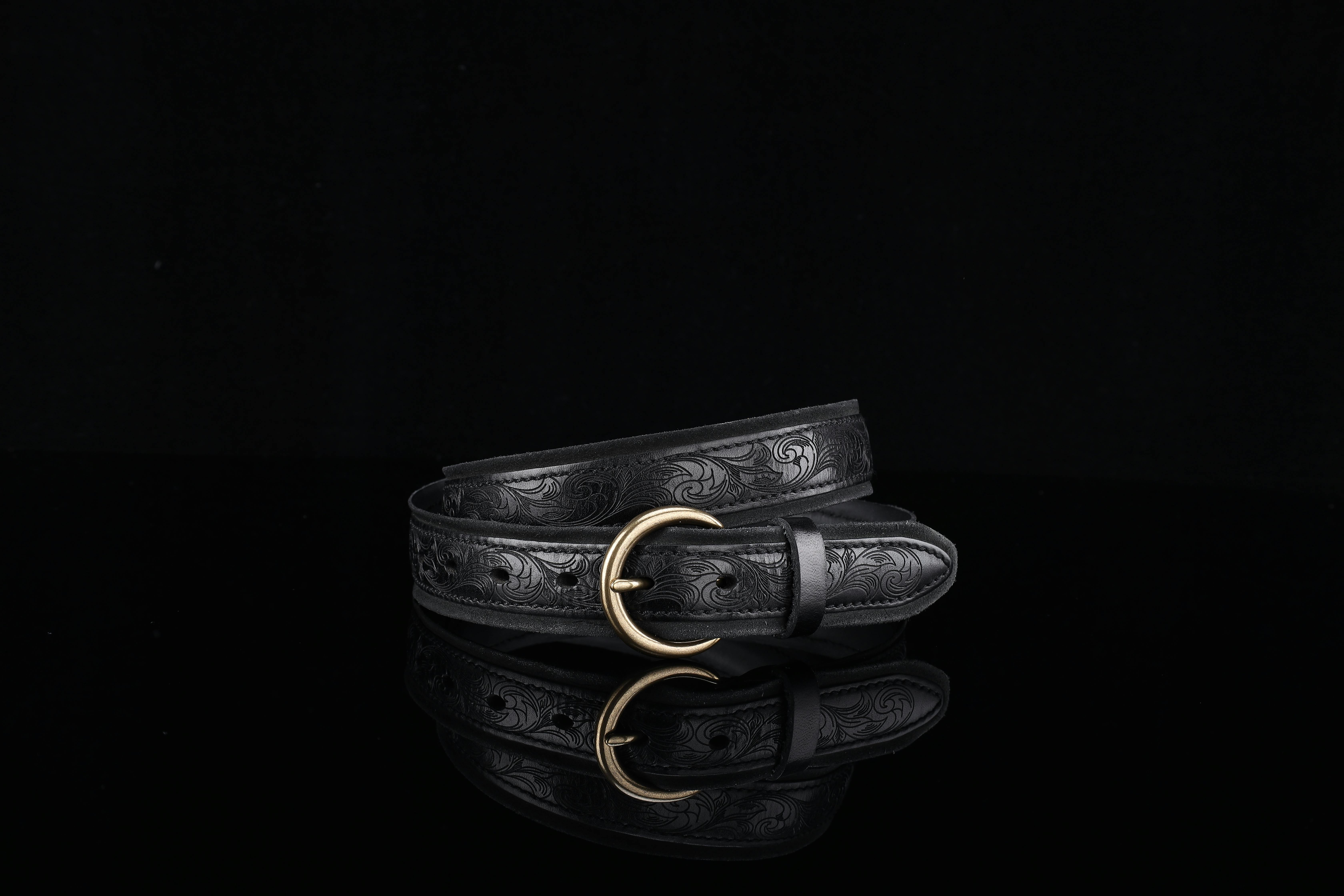 Free Stylish black leather belt with intricate embossing and brass buckle on black background. Stock Photo
