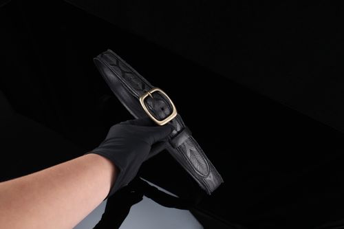 Free A sleek black leather belt with a gold buckle held against a dark background. Stock Photo