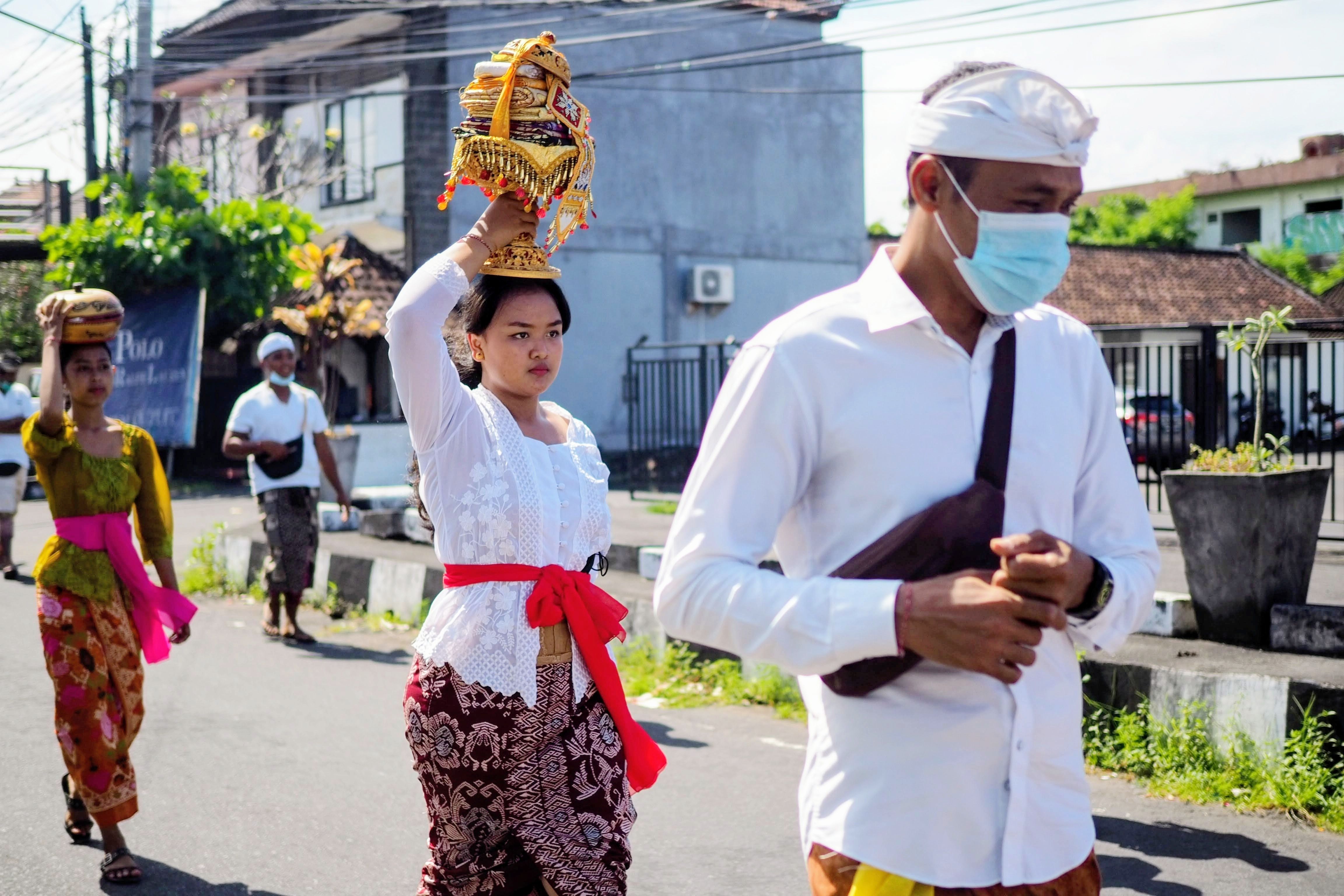 Một người Bali chăm sóc gà trống chiến bên hiên nhà, ánh chiều chiếu lên bộ lông đỏ