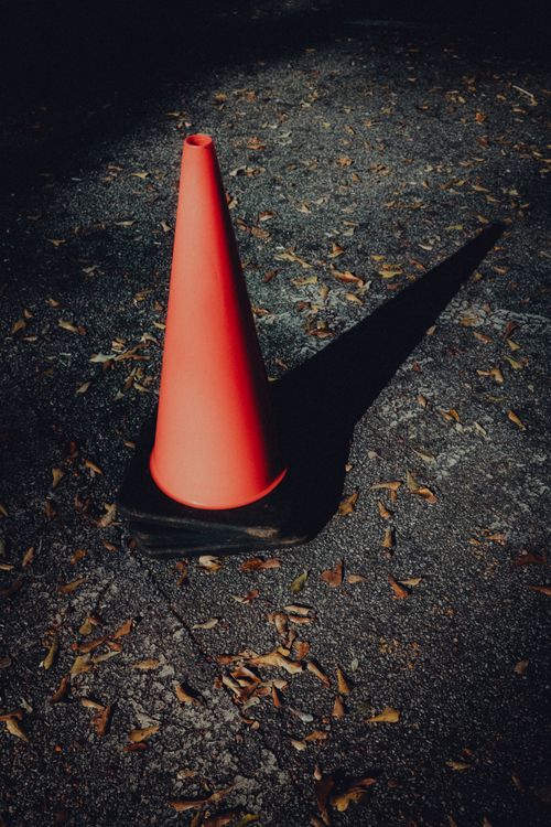 Free A solitary traffic cone casting a shadow on a leaf-strewn pavement in autumn light. Stock Photo