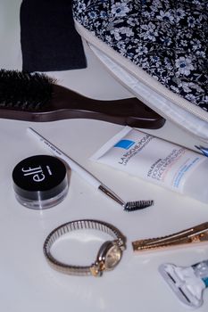 Flat lay of beauty essentials with a floral cosmetic bag, brush, watch, and makeup products.