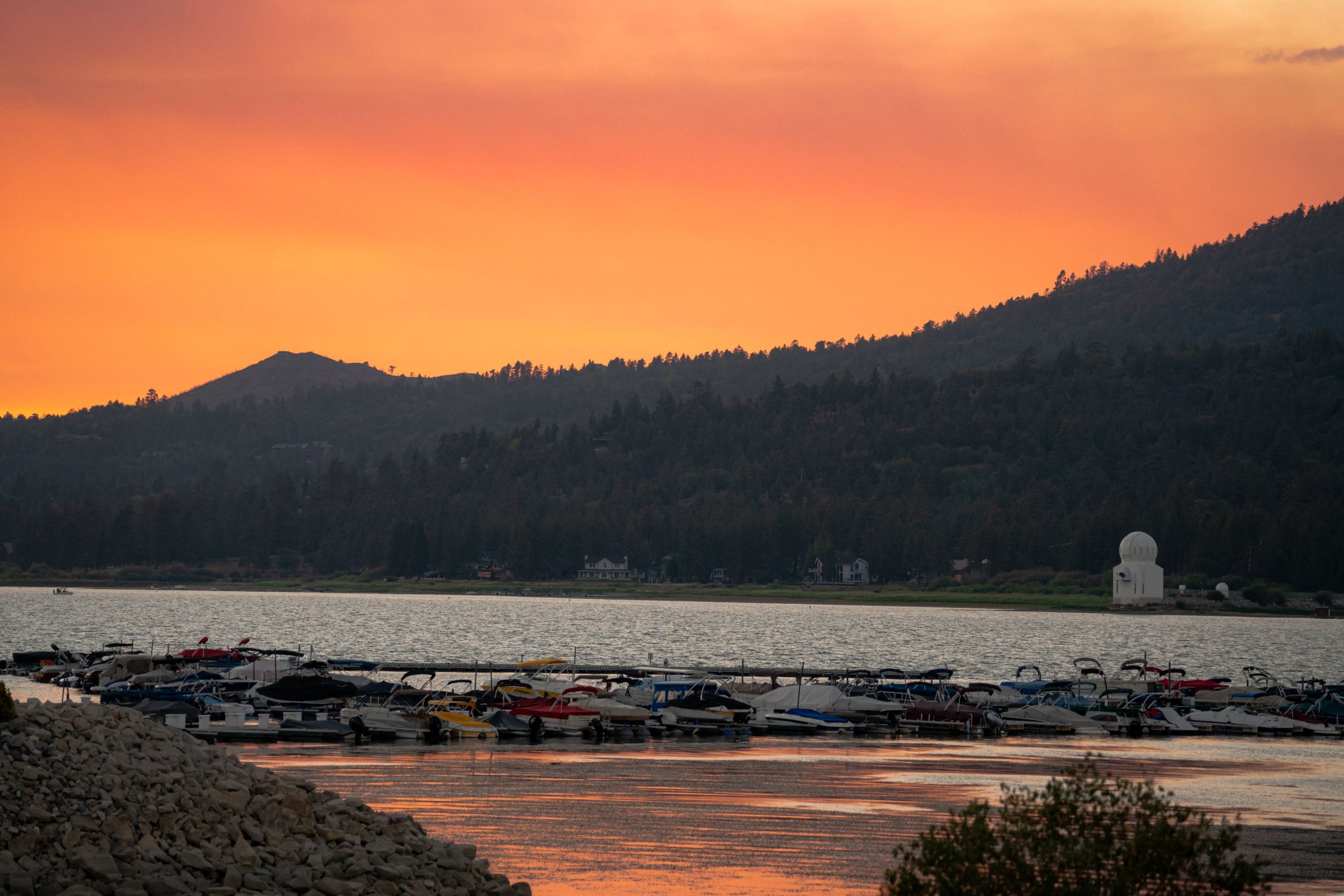 Stunning sunset view of Big Bear Lake, California with boats, mountains, and observatory in the backdrop.