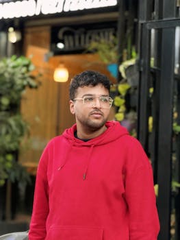 Portrait of a young man in a red hoodie standing outside a trendy café.