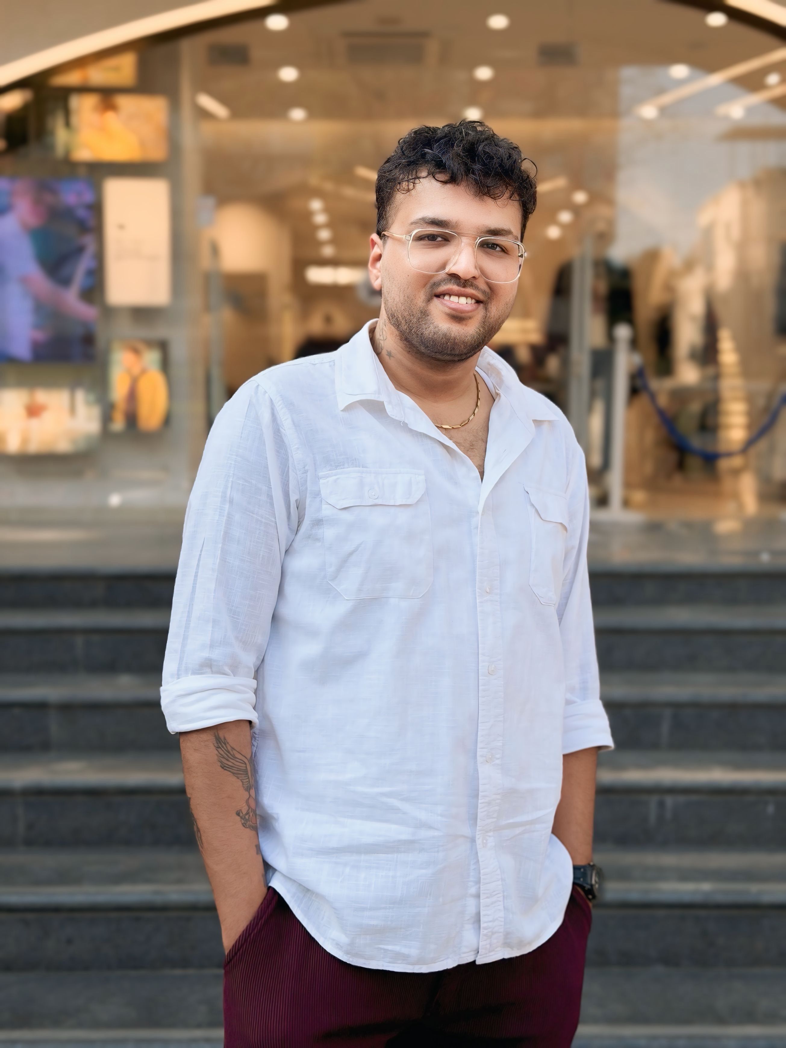 A man in a white shirt smiles confidently while standing outside an urban building.