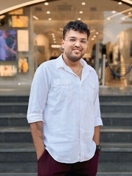 A man in a white shirt smiles confidently while standing outside an urban building.