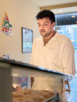 Adult male in a white shirt looking at pastries in a bakery. Warm and inviting atmosphere.